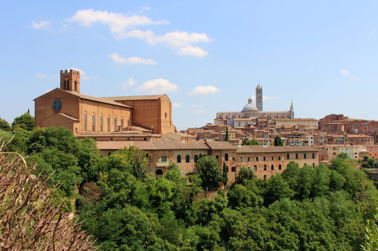 Gamle mursteinsbygninger i Siena omringer av frodig natur
