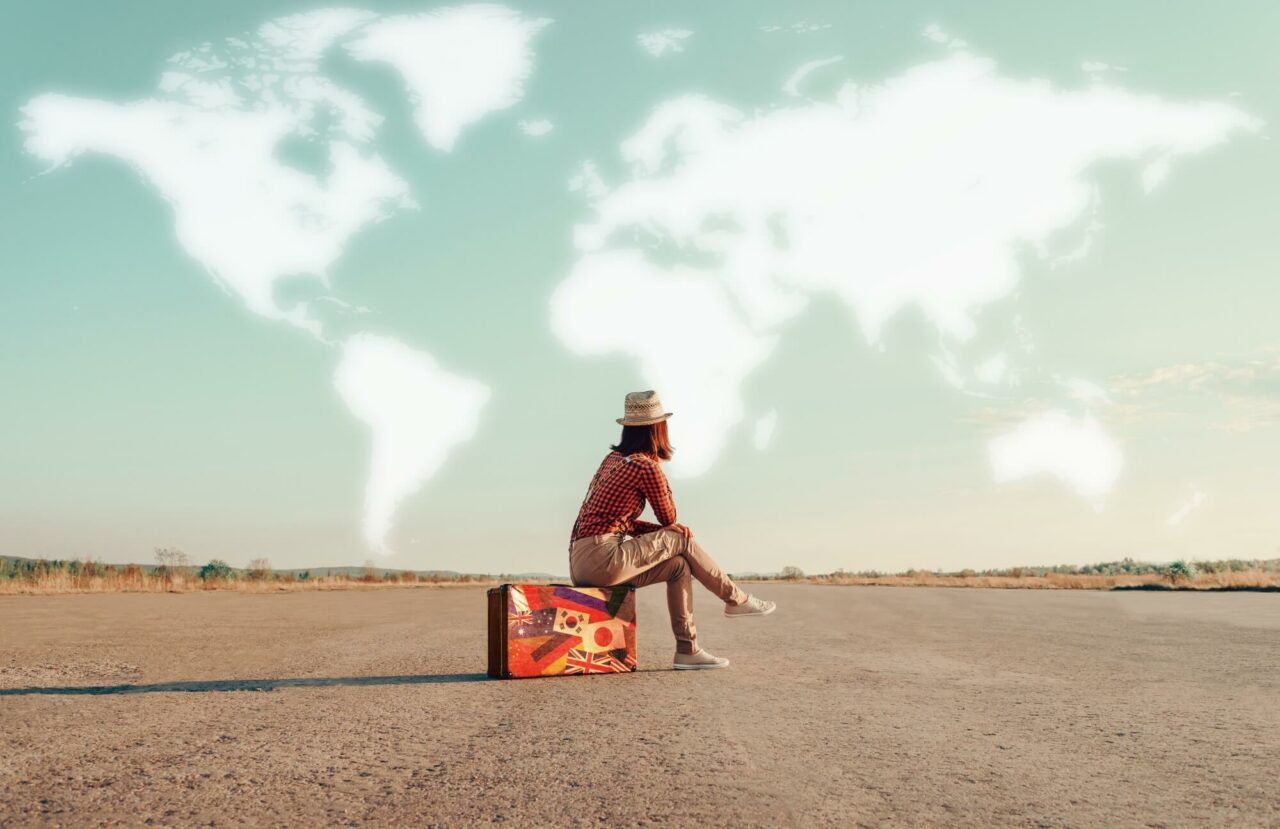 En jente sitter på en koffert og ser opp på et verdenskart