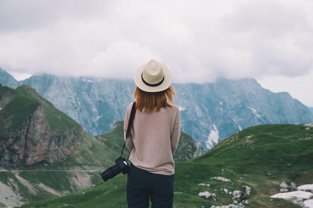 Ung kvinne ser utover fjellandskap med et kamera over skulderen