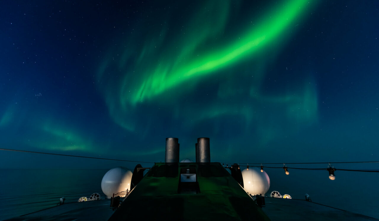 Grønt nordlys som danser på den mørke himmelen over Hurtigruten