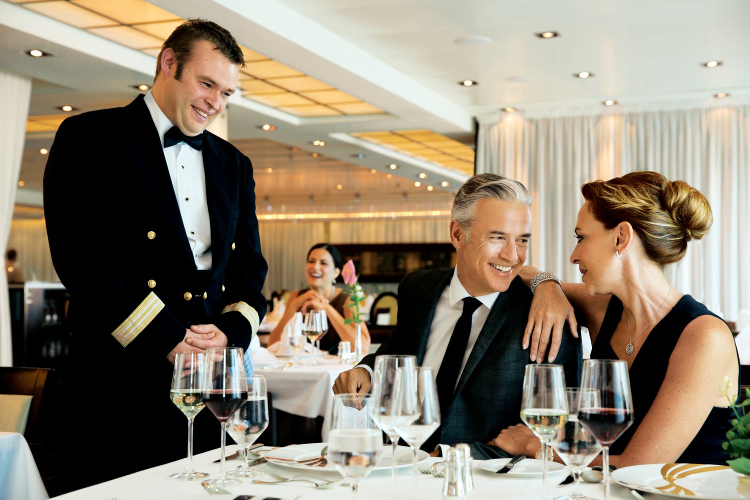 Par spiser en bedre middag om bord på et Seabourn-skip, med hovmesteren stående ved siden av bordet. Foto.