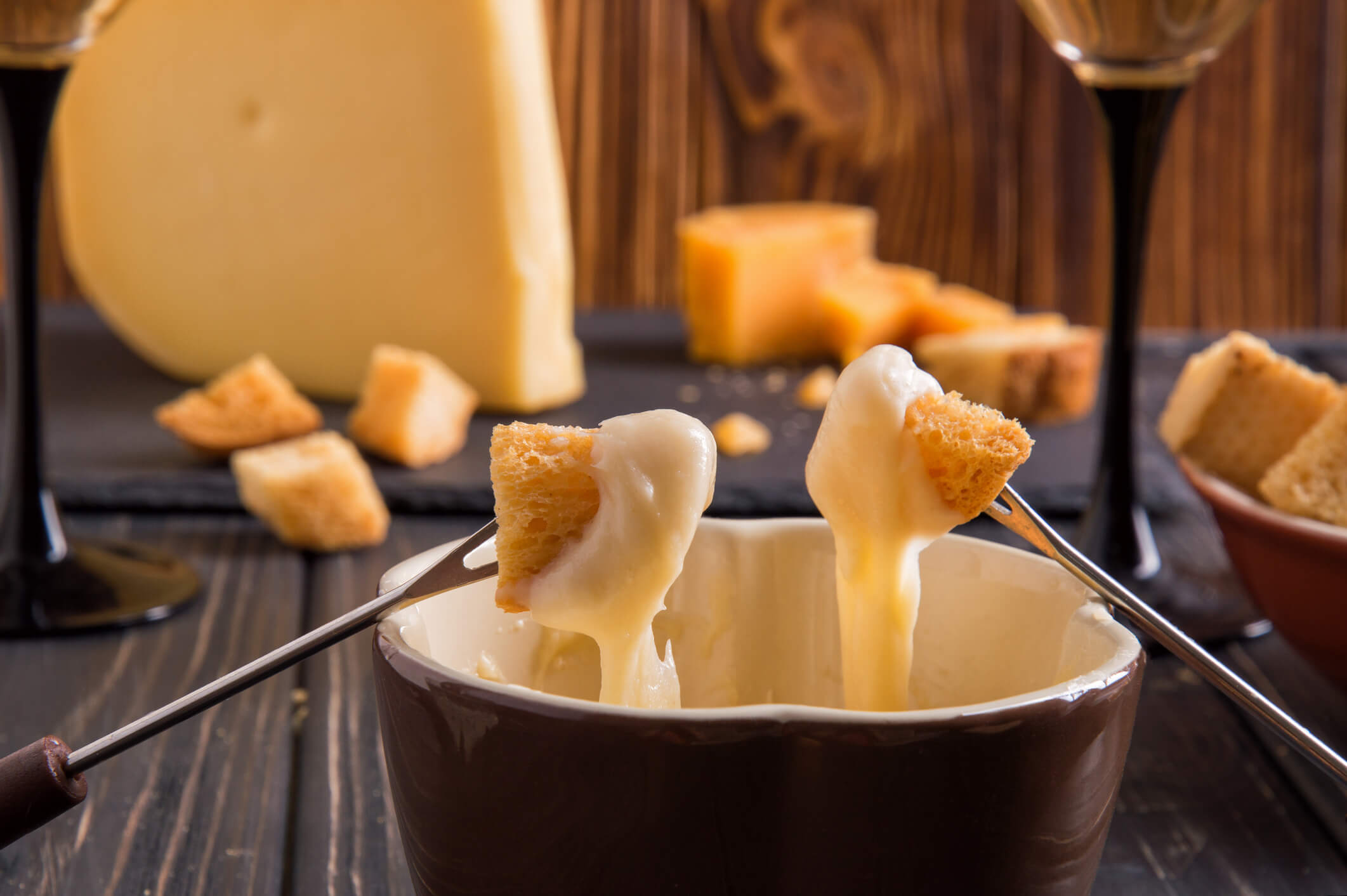 Nærbilde av Sveitsisk ostefondue og to pinner som dypper brødbiter i fonduen