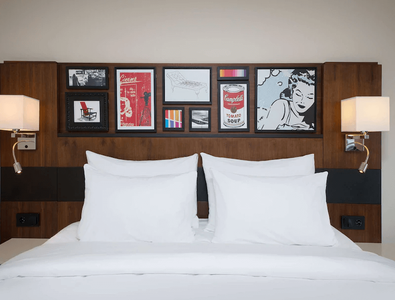 Bilde av et hotellrom med bilder over sengen og store hvite dunputer