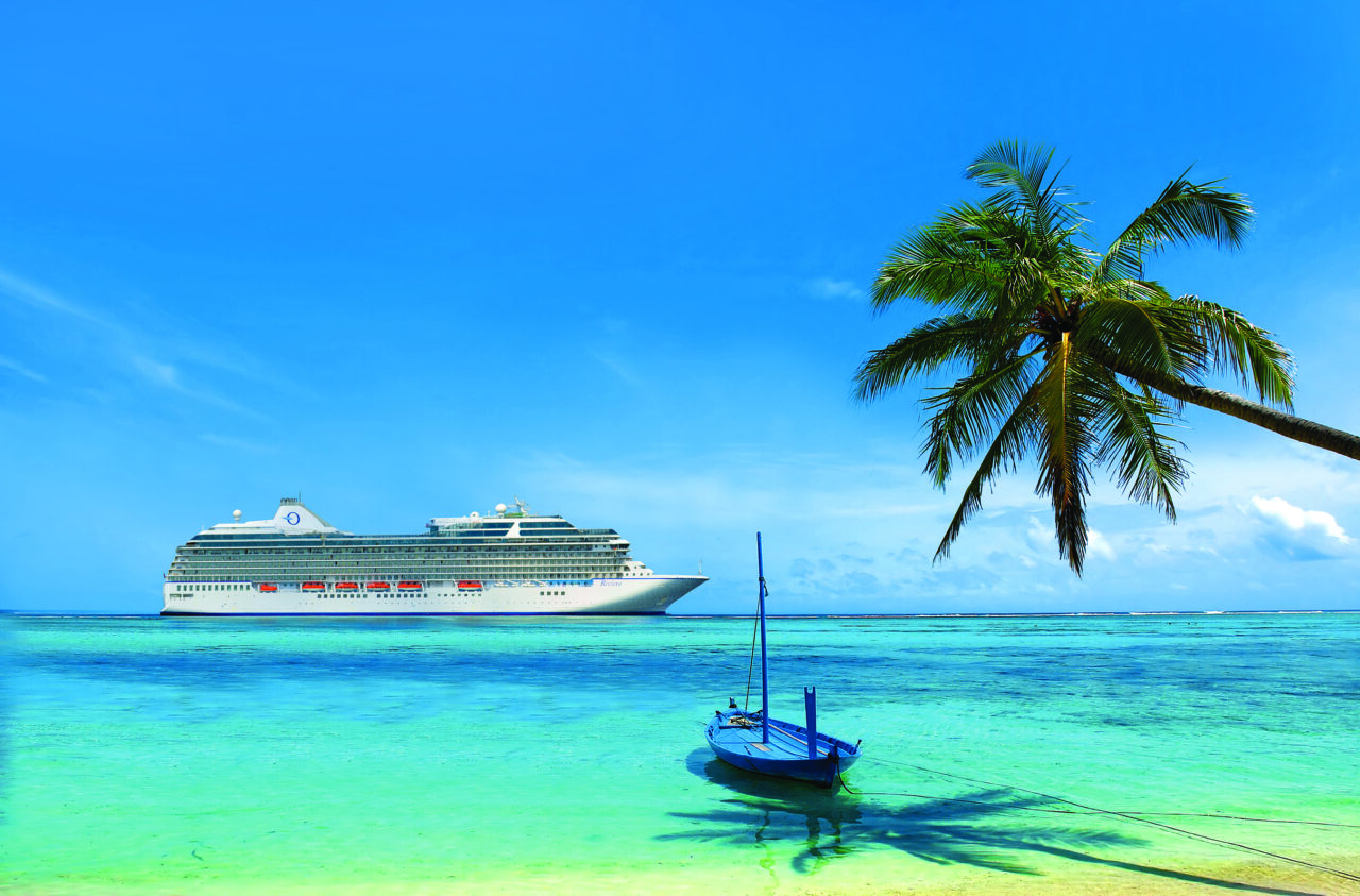 Et Oceania Cruises-skip på turkist hav utenfor en palmerik øy i Karibia. Foto.