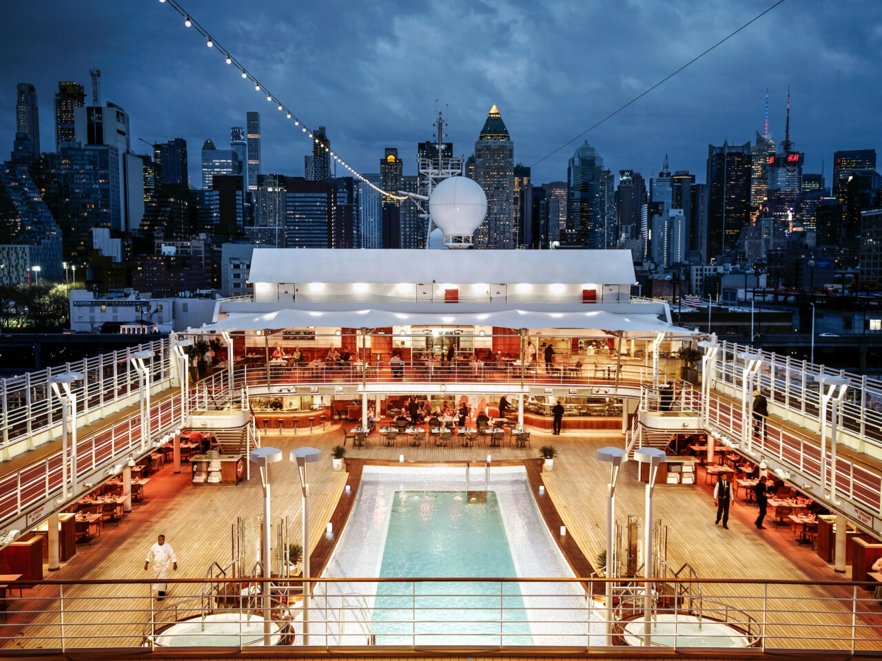 Kveldsbilde av bassengdekket om bord på Silver Muse, med Manhattan, New York, i bakgrunnen. Foto.