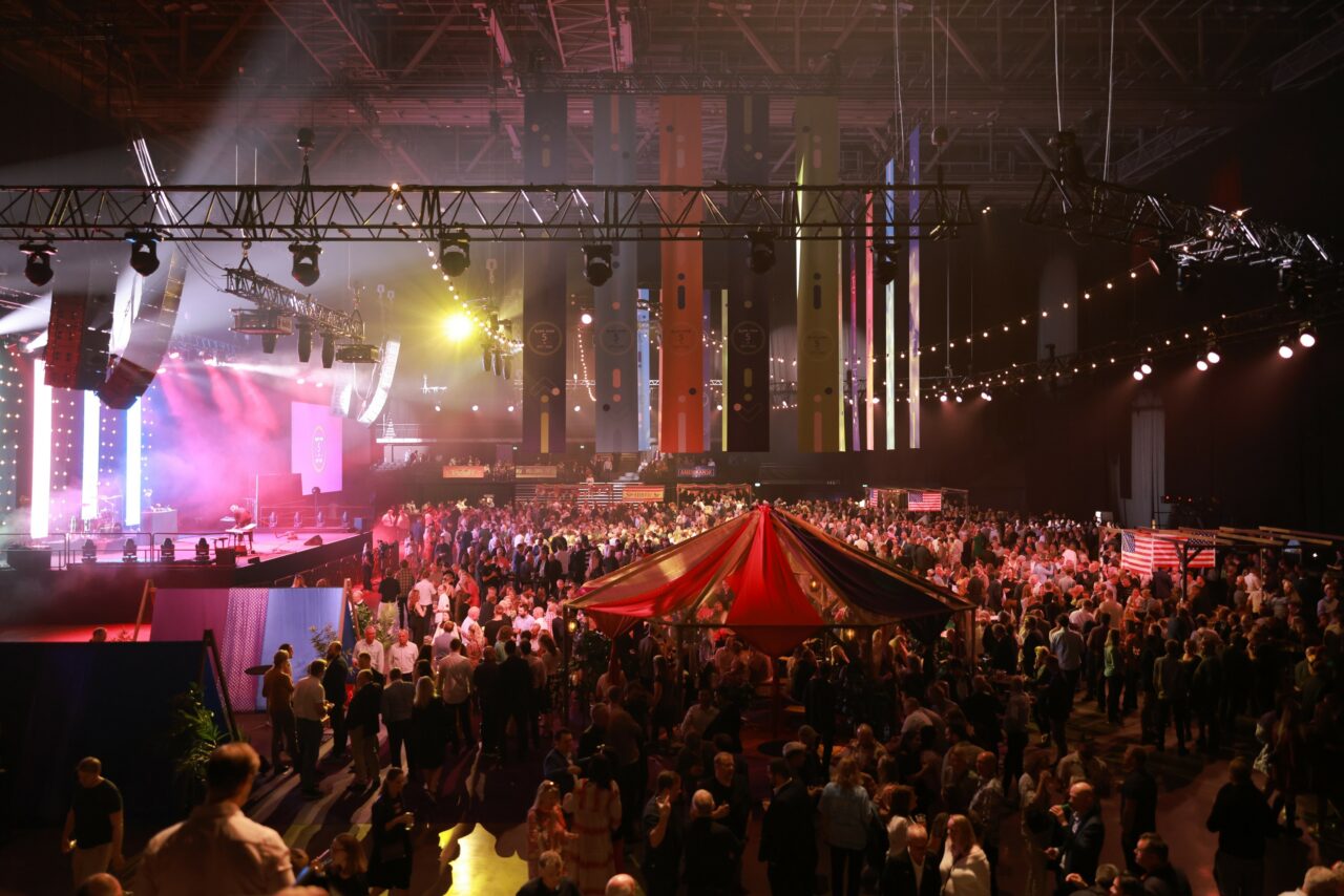 Flere tusen mennesker i en stor festsal med scene foran. Foto