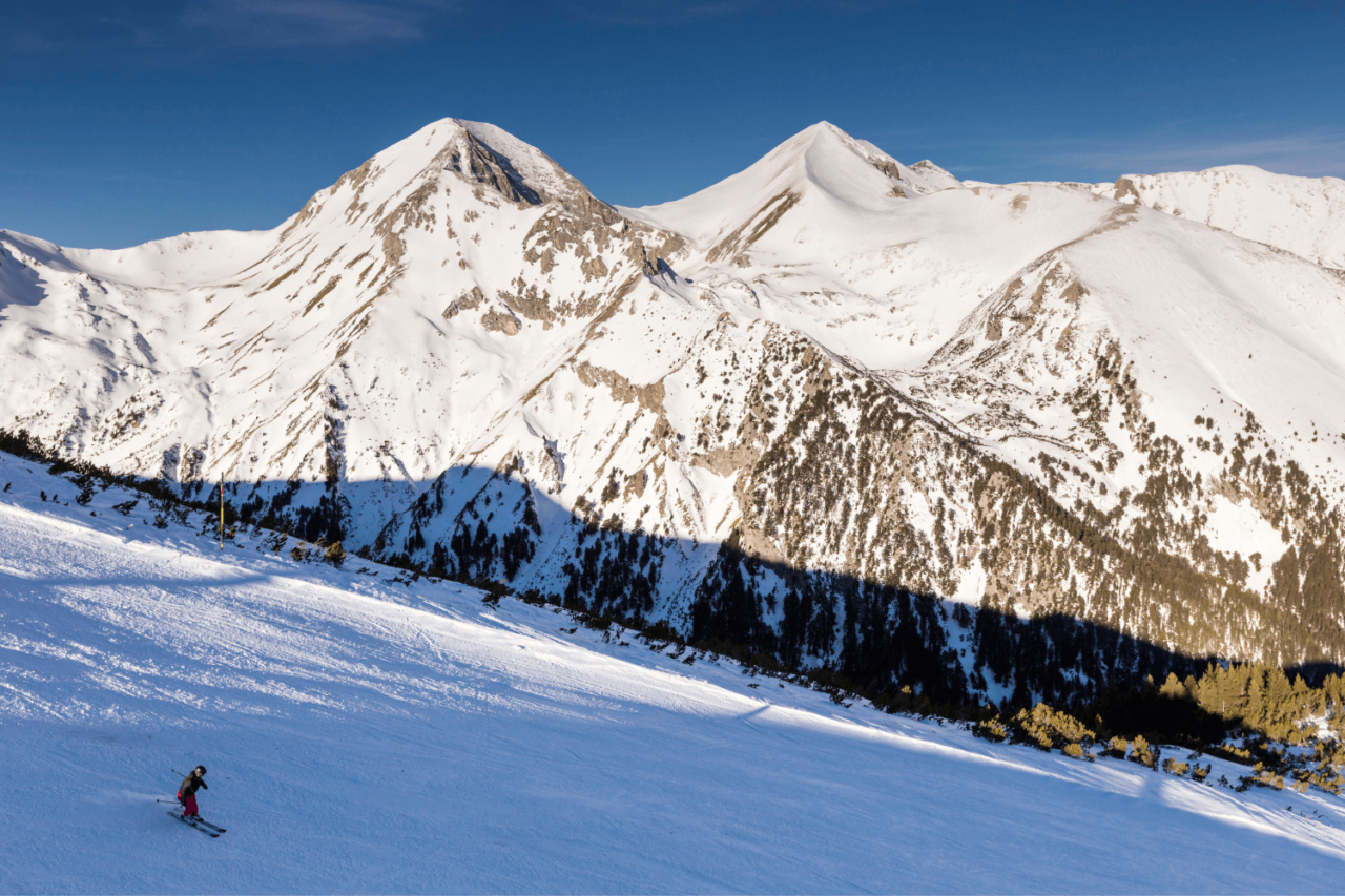 En som kjører ned slalåmbakken på ski blant høye fjell. Foto