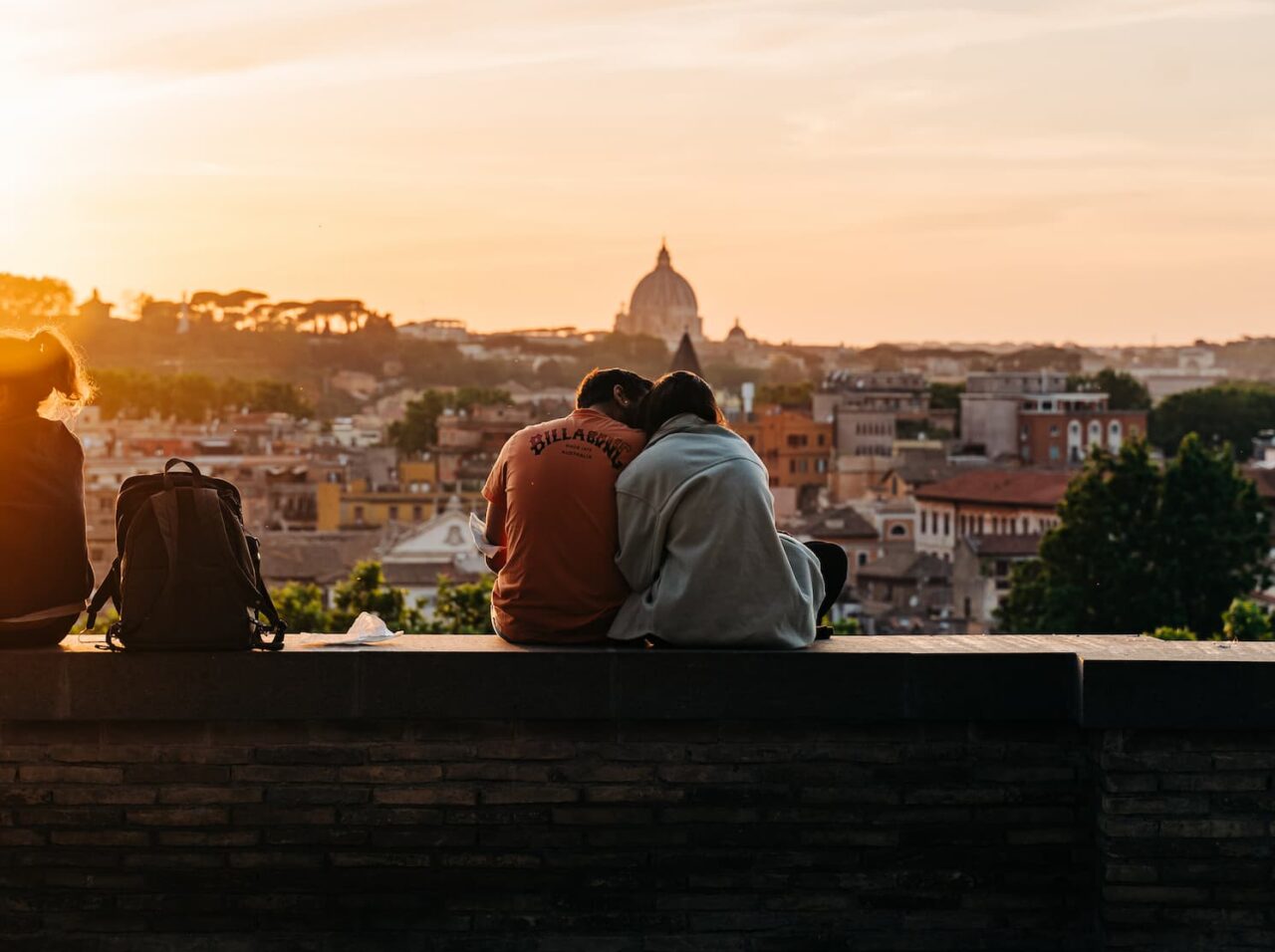 To mennesker sitter med ryggen til og ser ut over en by i solnedgang. Foto