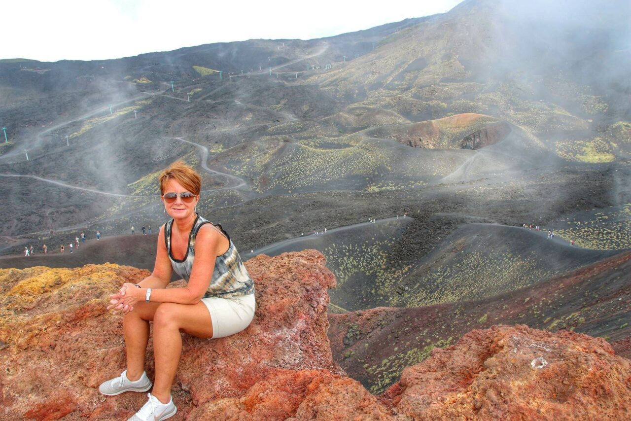 Kvinne sitter på en stein med lavalandskap rundt. Foto