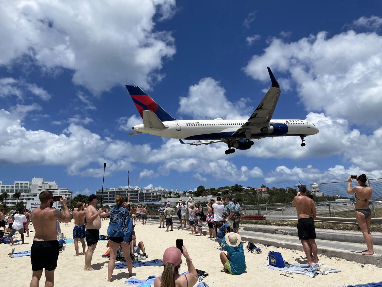 Mennesker står på en strand hvor et fly tar av rett over hodene deres. Foto