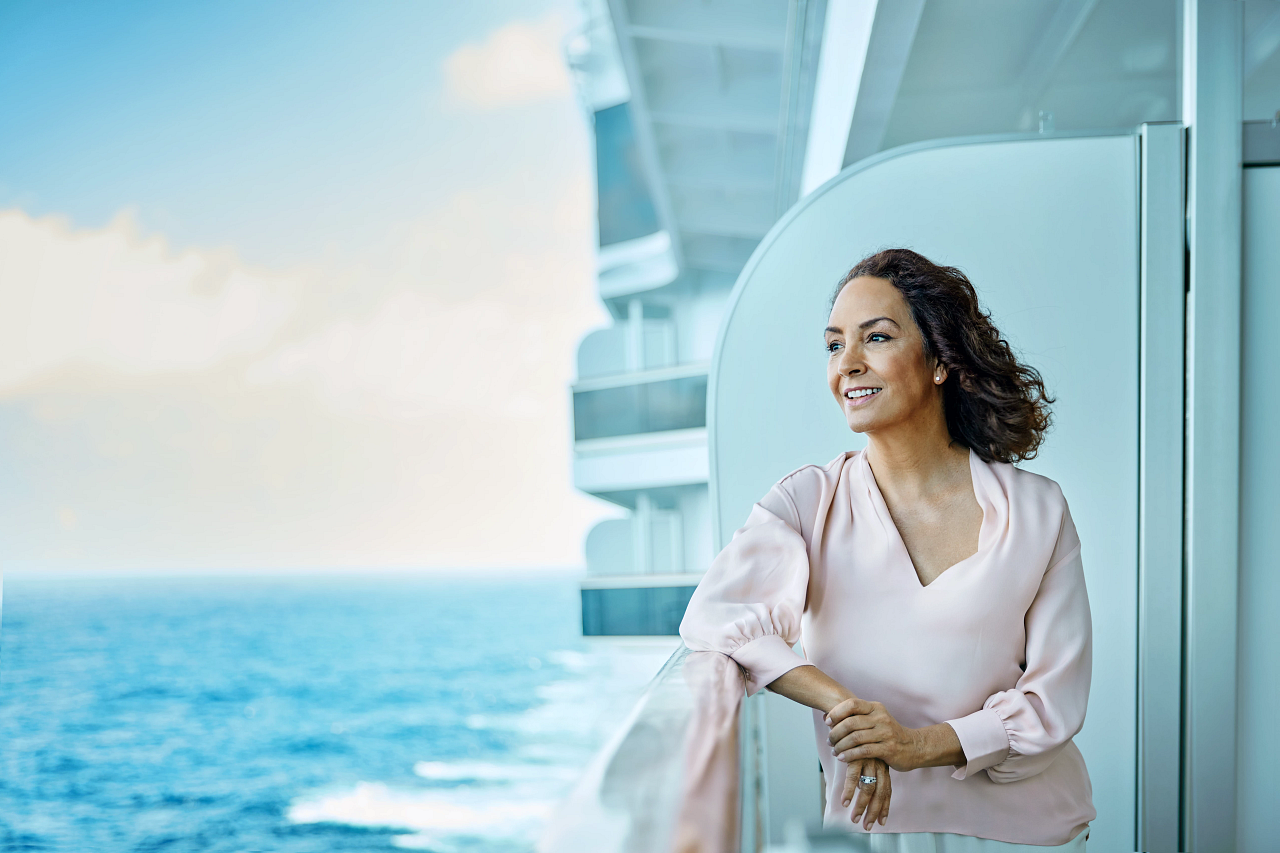 Kvinne ser utover havet fra balkongen om bord på et cruiseskip. Foto.