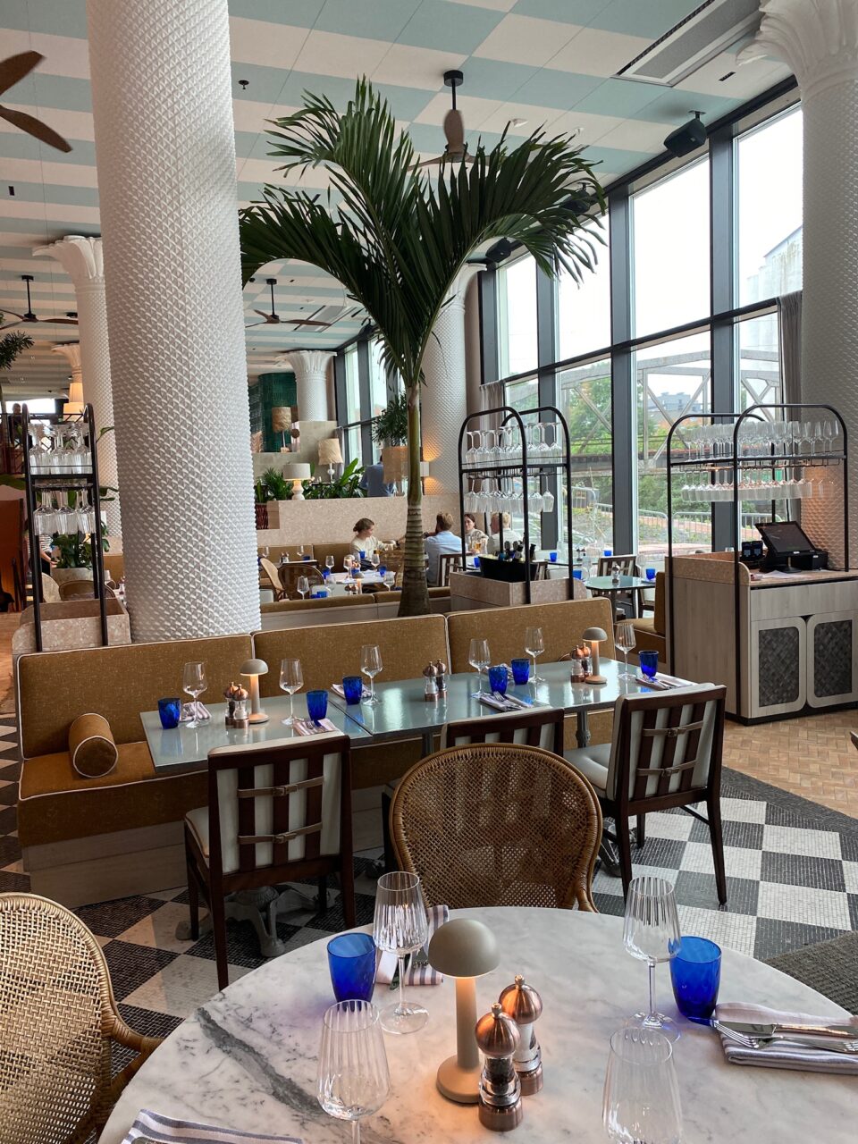 Et hyggelig spiseområde med hvite gipssøyler, palmer og pent dekkede bord. Foto