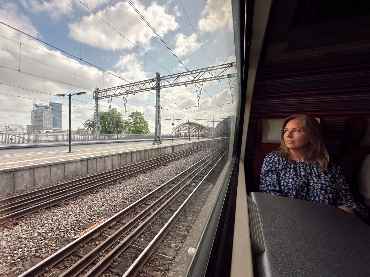 Kvinne sitter på et tog og ser ut vinduet på togskinnene. Foto