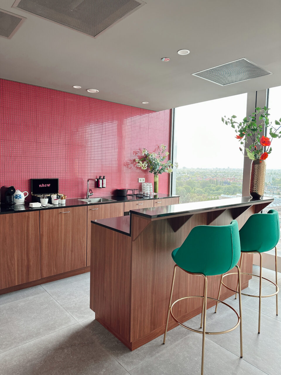 Et kjøkken med rosa fliser, grønne stoler og detaljer i tre. Foto