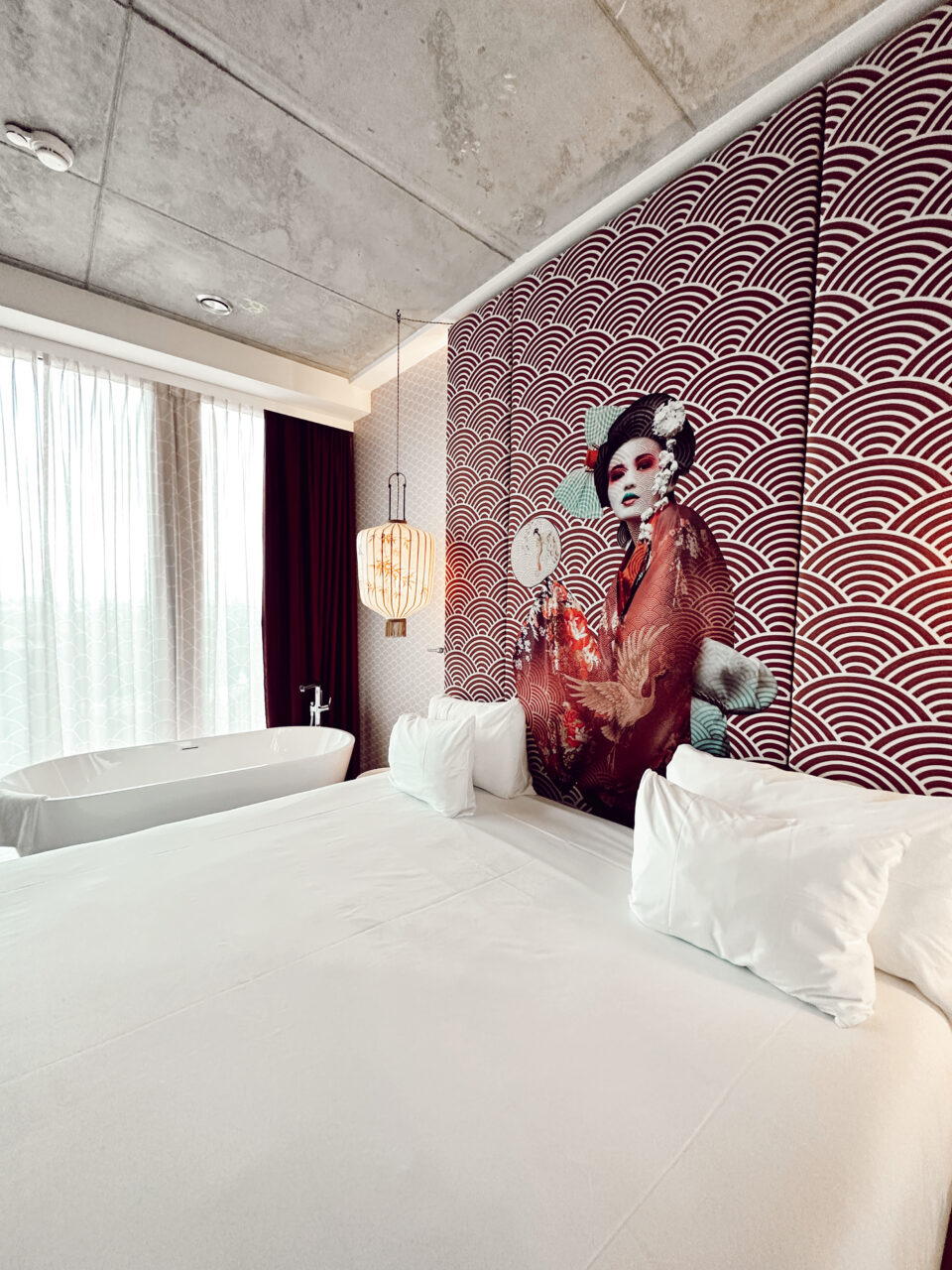 Et hotellrom med kunst av en dame på veggen, dobbelseng og badekar med utsikt ut vinduet. Foto