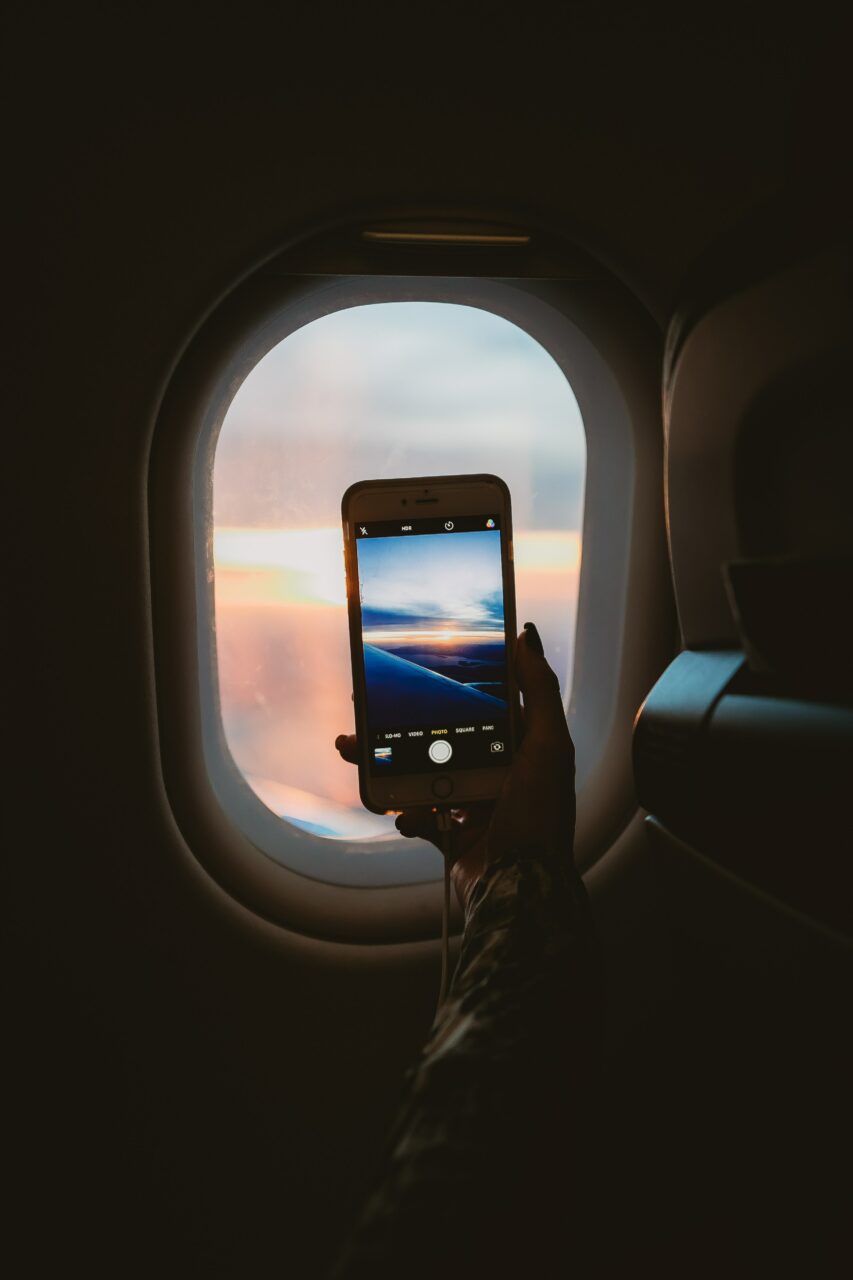 En telefon som tar bilde ut et flyvindu i soloppgang. Foto