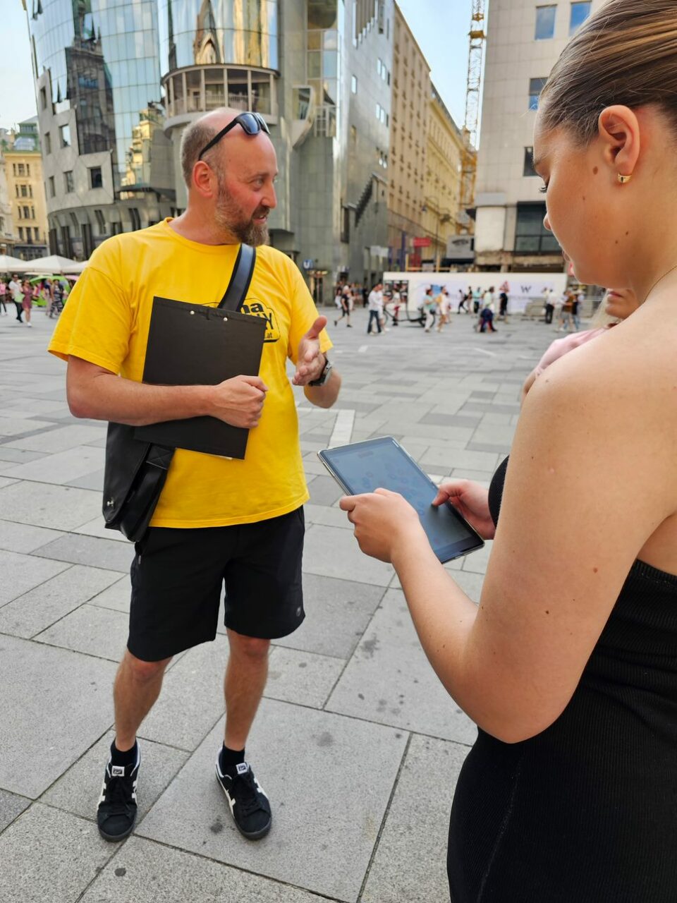 Kvinne står og ser ned i en iPad mens hun får instruksjoner av mann. Foto
