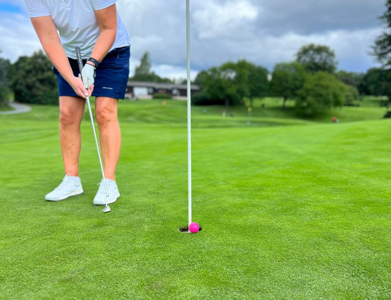 Person står på grønn plen med golfkølle i hånden og klar til å treffe golfballen. Foto