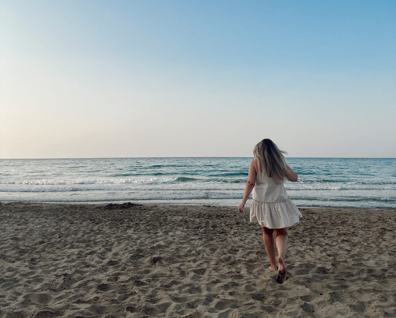 En jente som løper på en strand mot havet. Foto