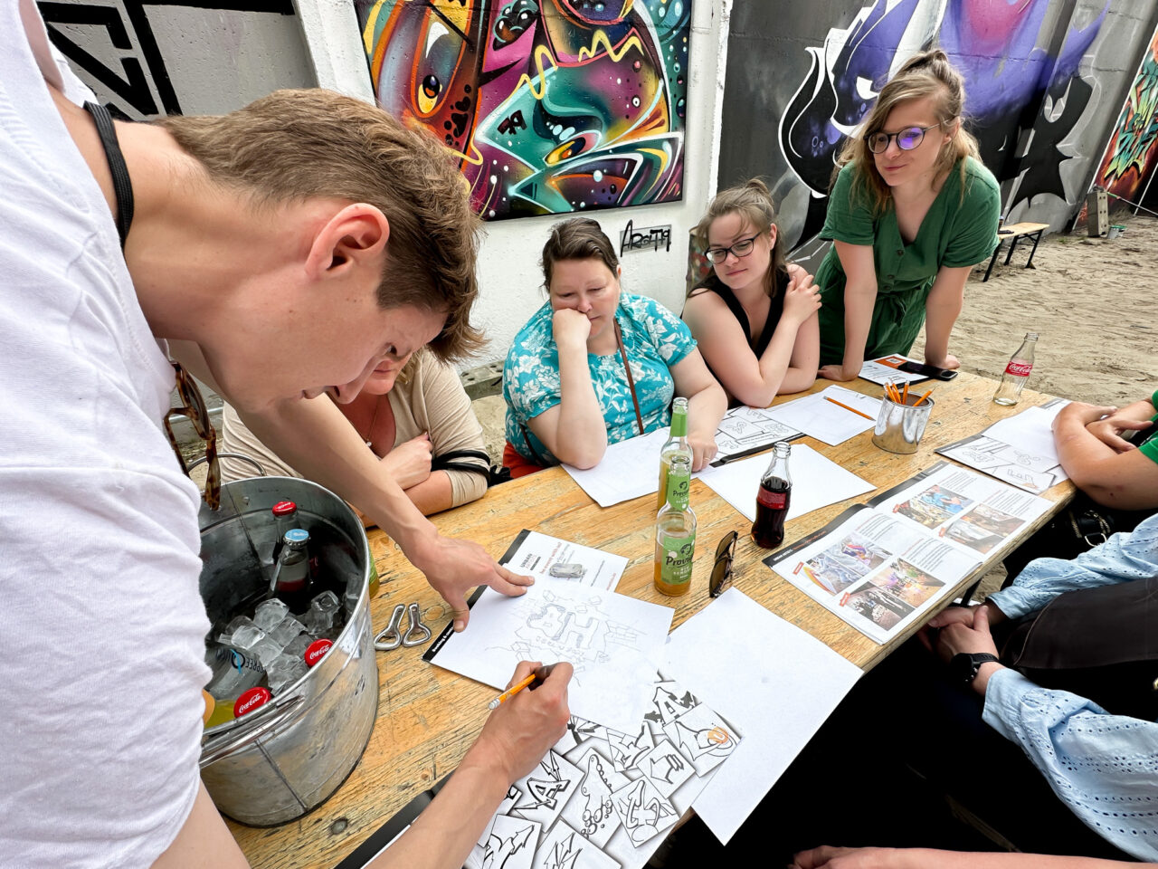 En gruppe mennesker som sitter rundt et bord og ser på en mann tegne på et ark. Foto