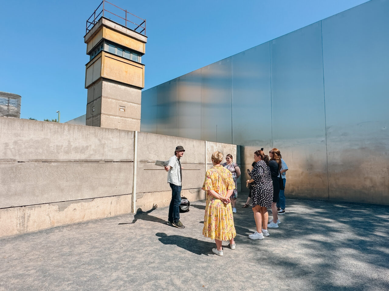 En gruppe mennesker som står foran Berlinmuren og et utsiktstårn. Foto