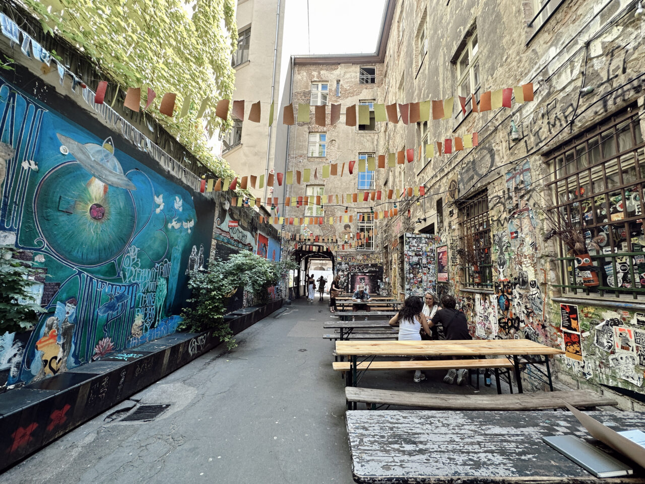 En bakgård med nedtaggede vegger og kunstverk. Det er satt opp benker hvor folk sitter. Foto