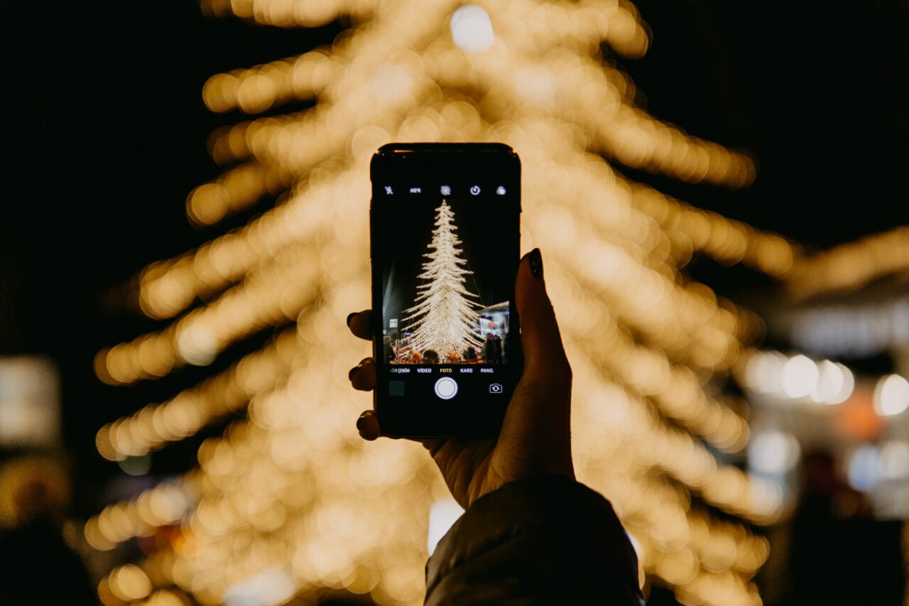 Person holder opp en telefon og tar bilde av et juletre. Foto