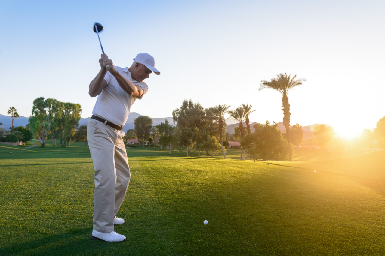 Golfspiller svinger golfkøllen mens solen går ned i horisonten. Foto