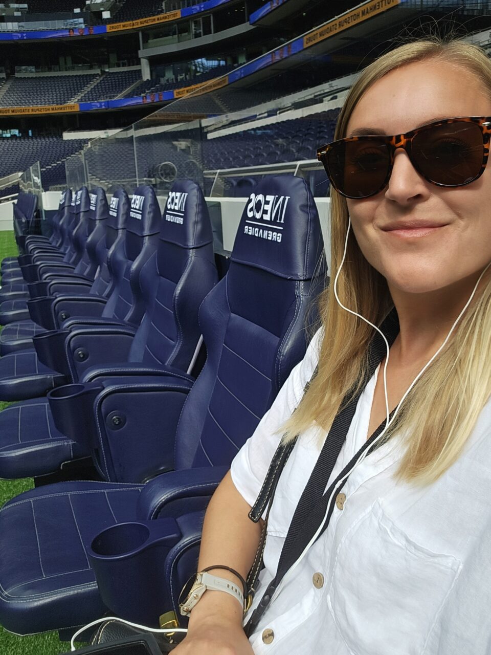 Kvinne sitter og lytter til guide i ørepropper på sidelinjen på stadion. Foto