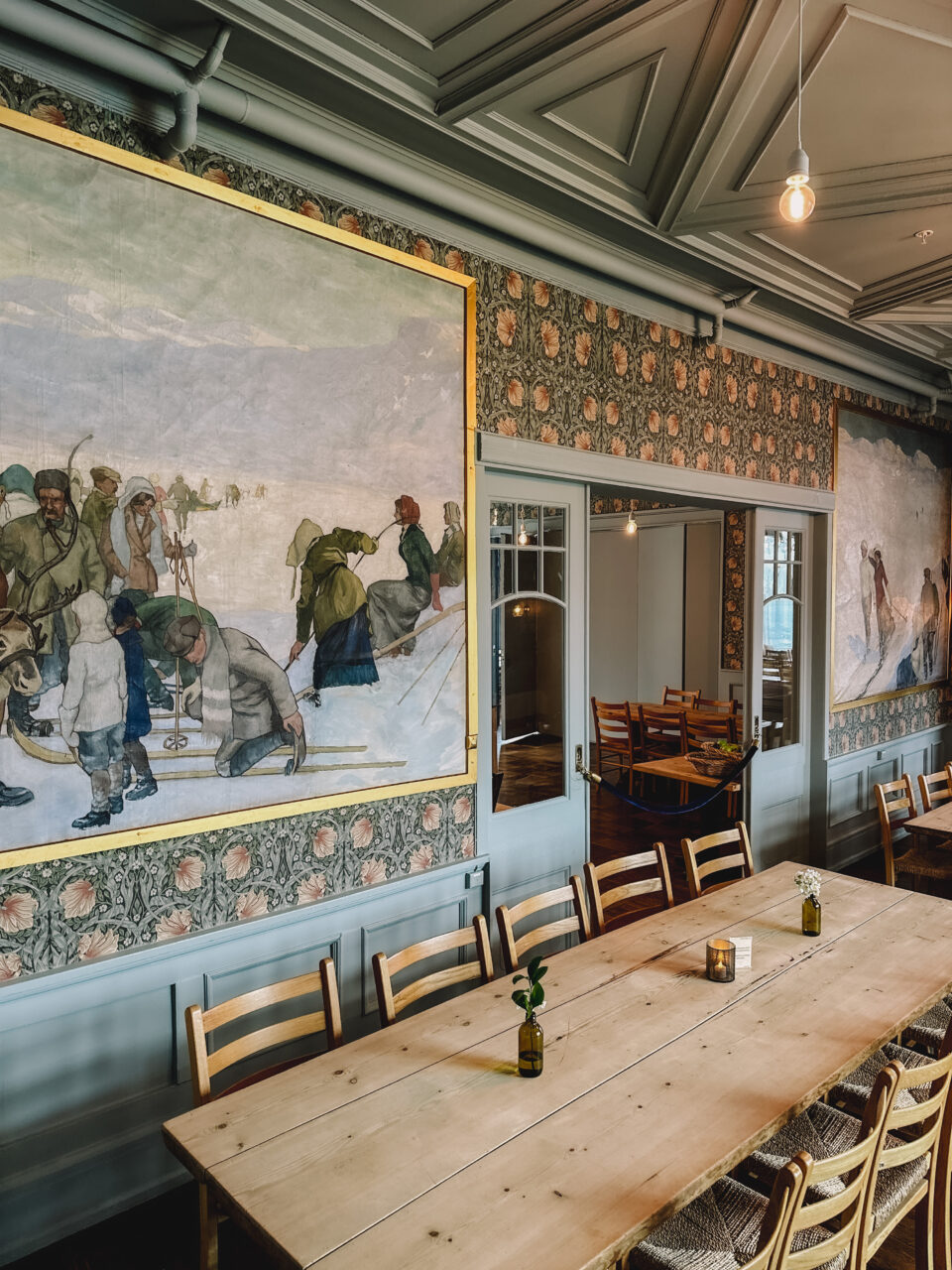Et langt spisebord i et hyggelig lokale med flotte maleri på veggen. Foto