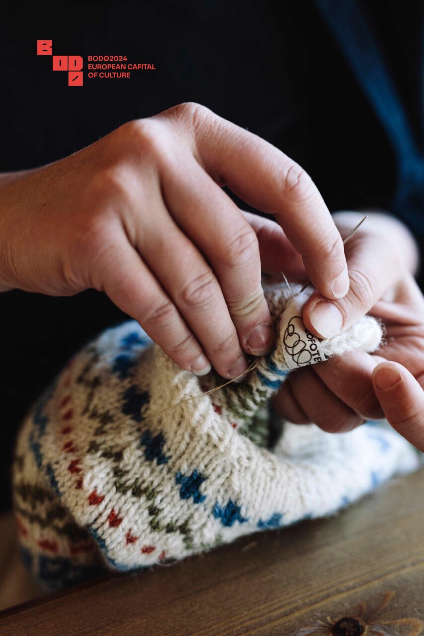 En hånd som syr en lapp på en strikket genser. Foto