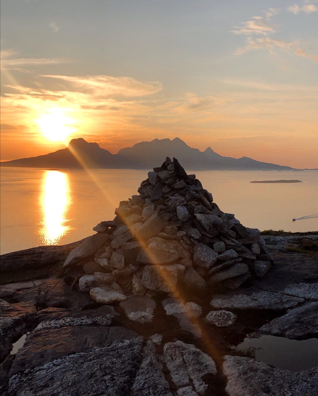 Utsiktsbilde utover havet og en steinknaus mot en solnedgang. Foto
