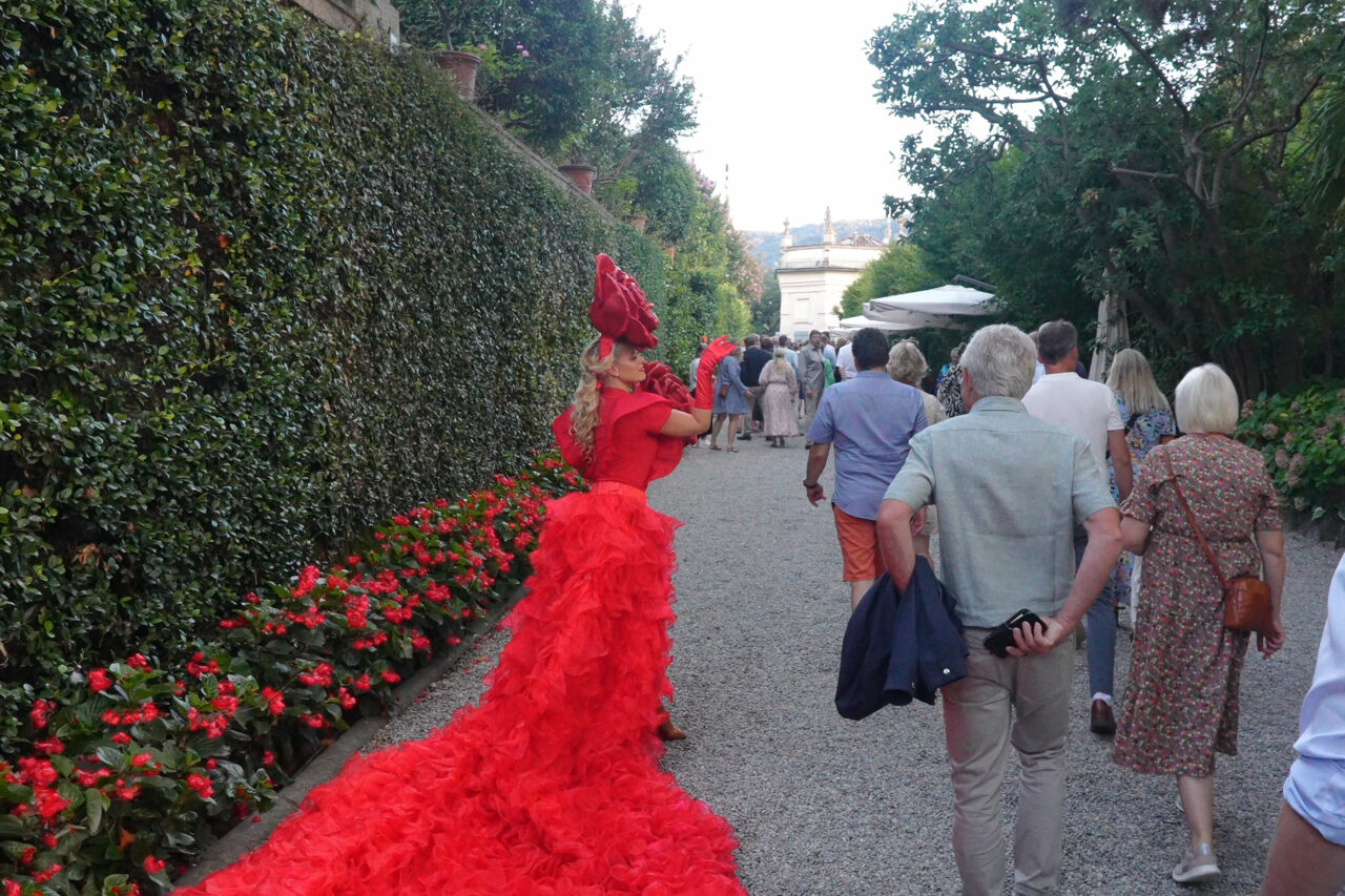 Mennesker går innover en grusvei sammen med en kvinne kledd i rød kjole. Foto