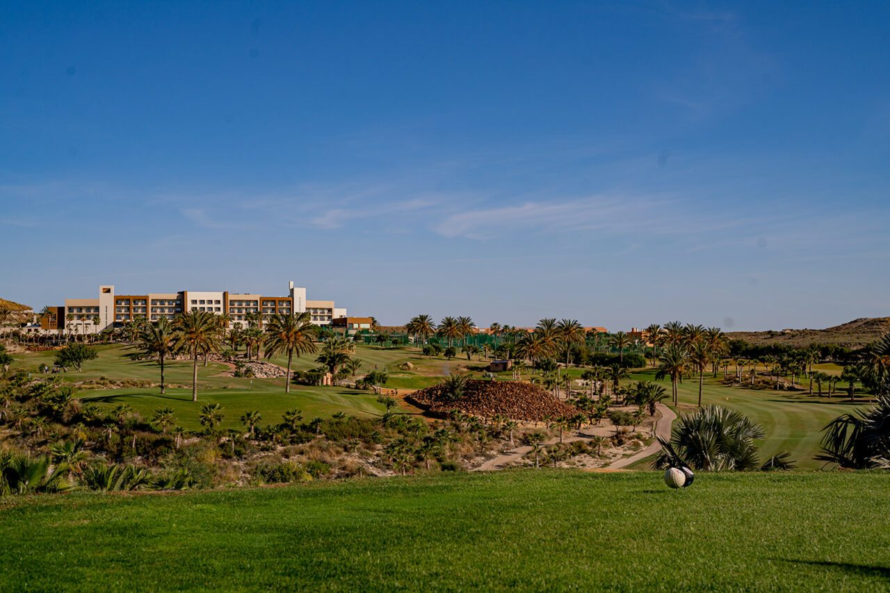 Stor og grønn golfbane med hotell i bakgrunnen. Foto