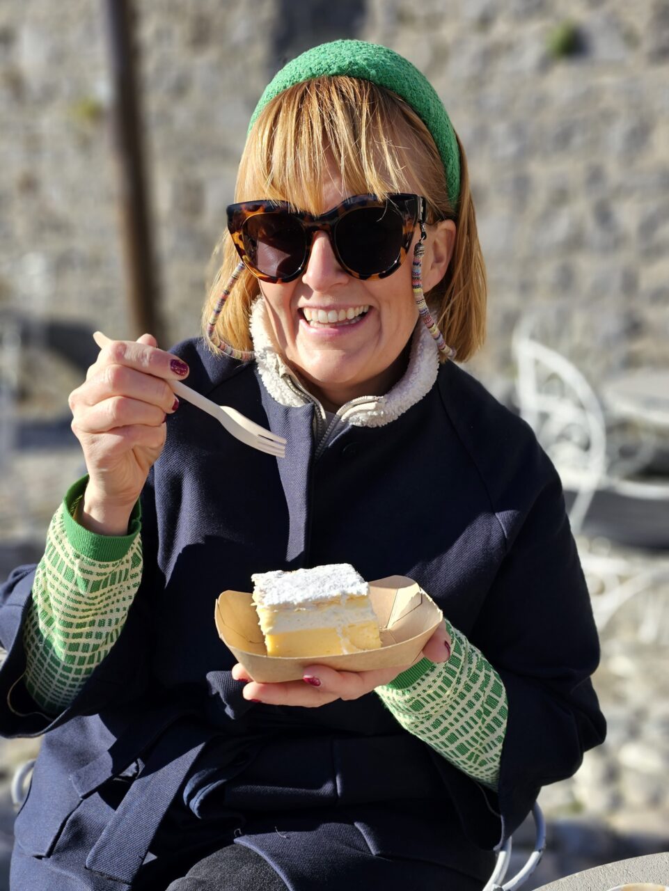 Kvinne smiler mens hun spiser kremkake i solen. Foto