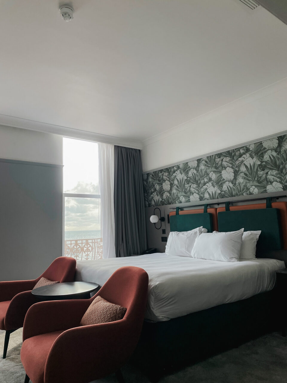 Dobbeltseng på hotellrom med grønne toner og vindu med utsikt. Foto