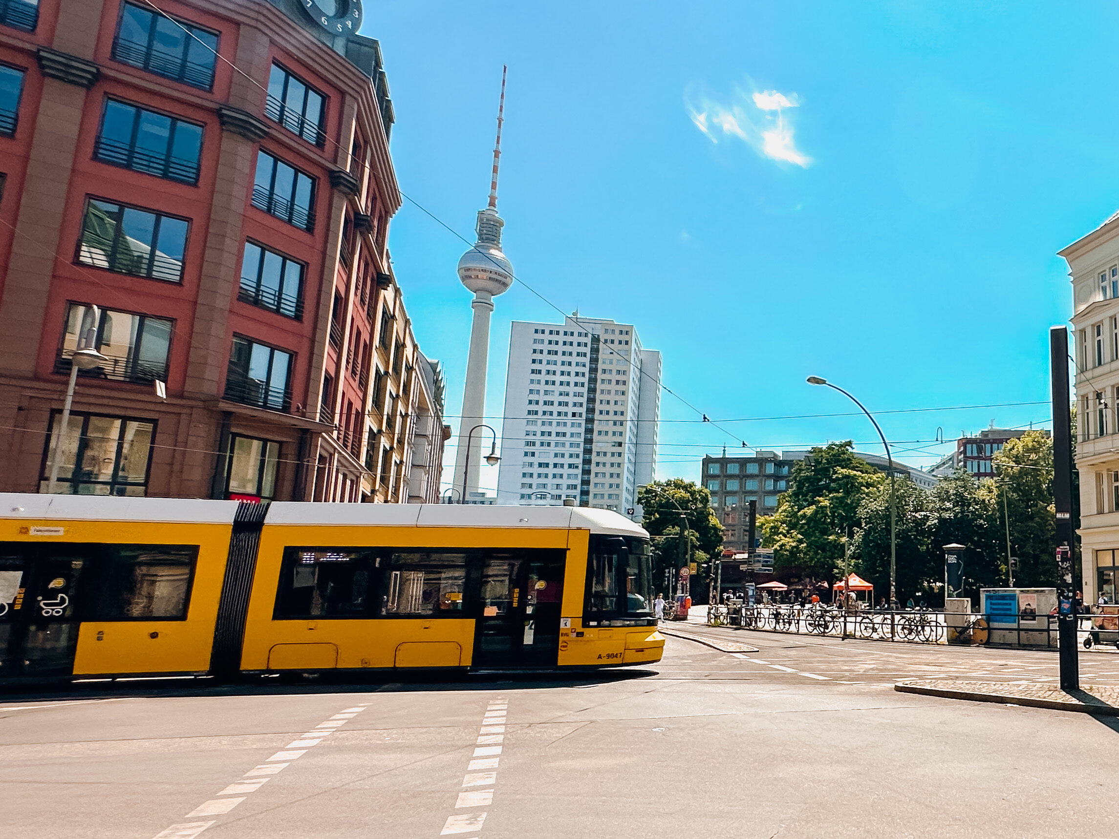 En gul trikk som kjører over et veikryss i Berlin med TV-tårn i bakgrunnen. Foto