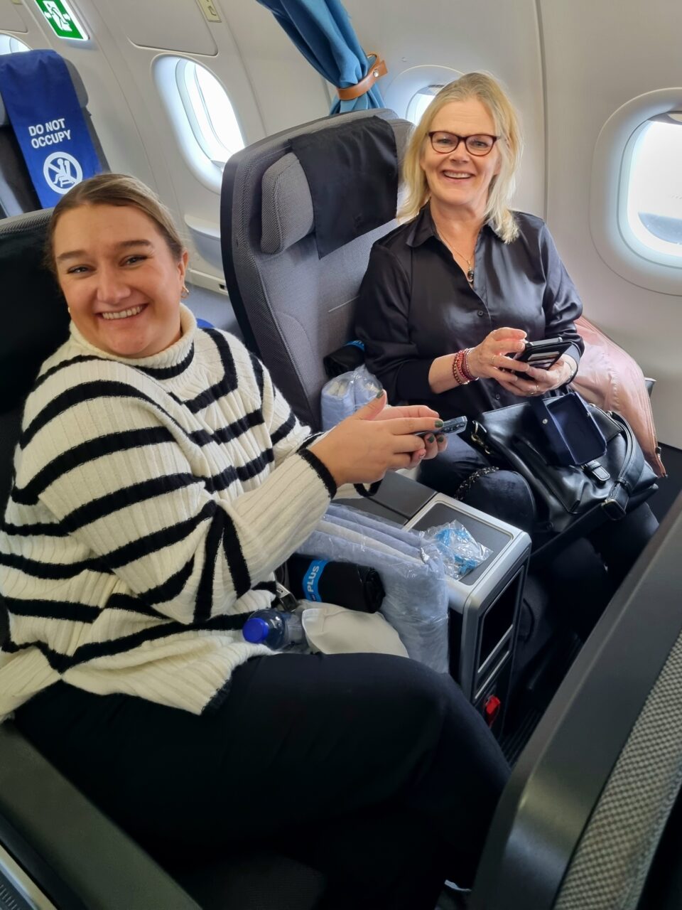 To kvinner smiler inn i kamera mens de sitter på fly. Foto