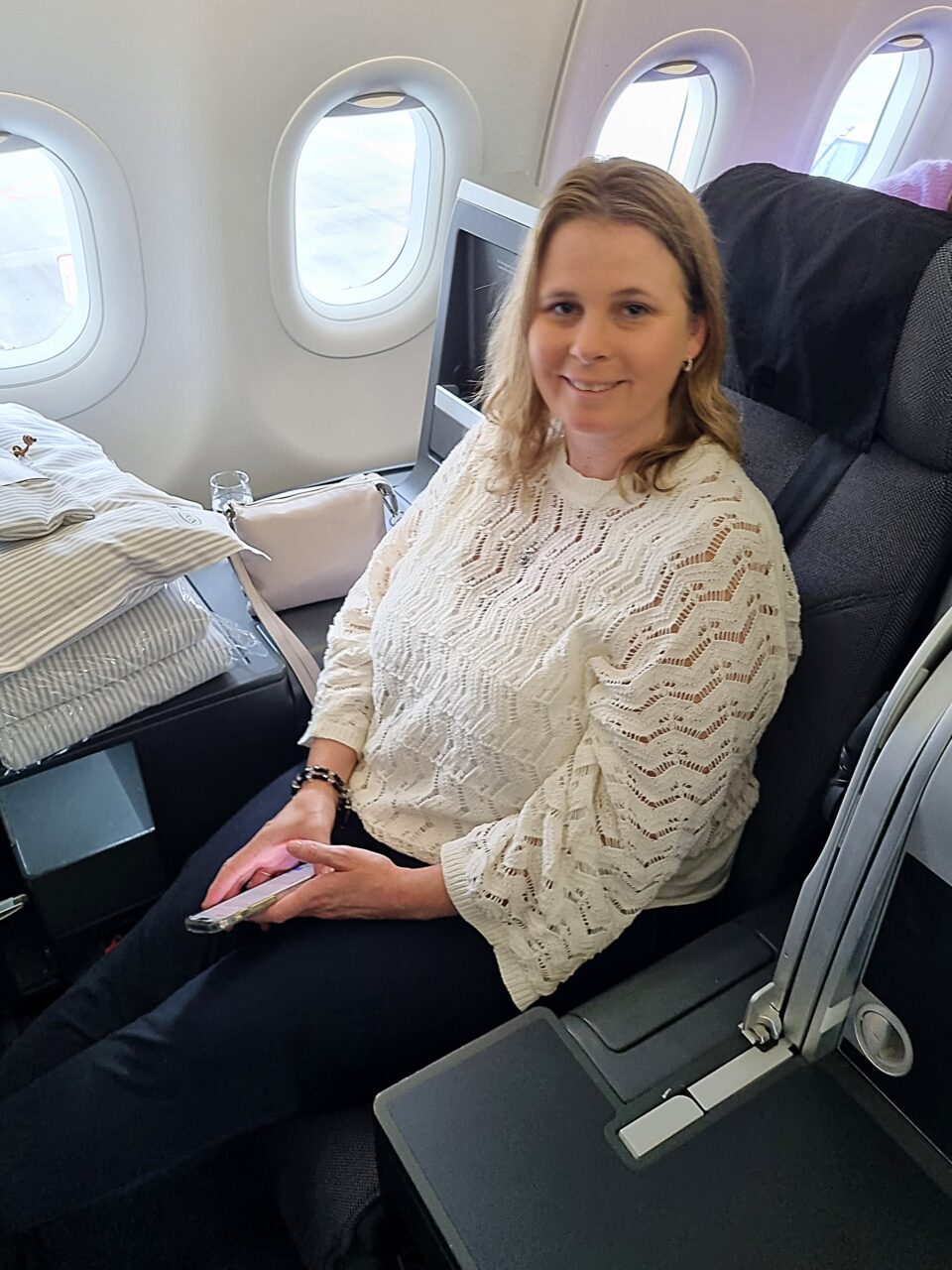 Kvinne sitter om bord fly i et stort og komfortabelt sete. Foto