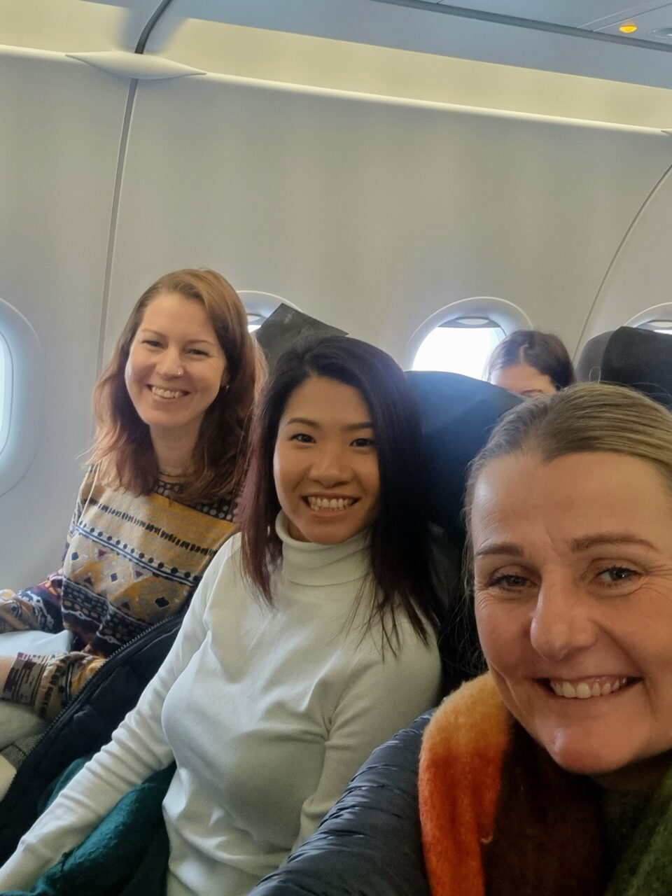 Tre kvinner smiler inn i kamera mens de sitter på fly. Foto