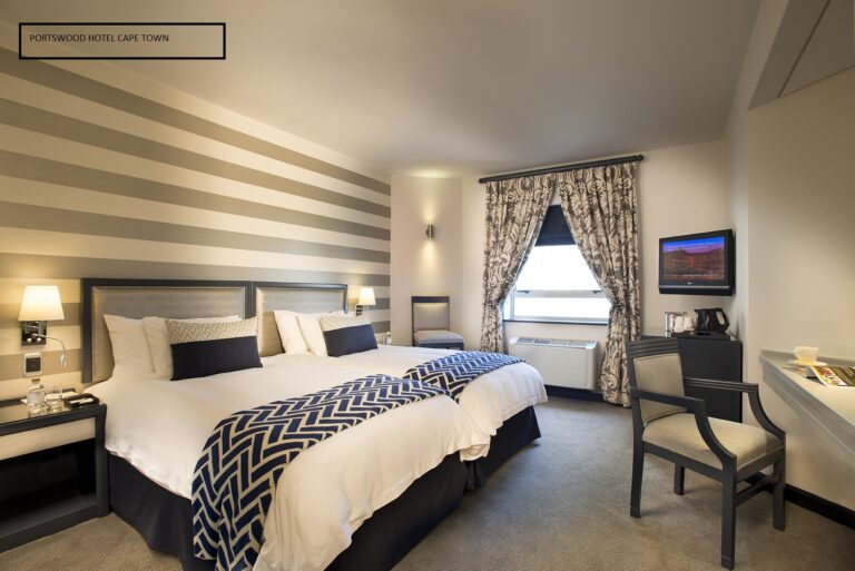Hotellrom med 2 senger, hvitt sengeteppe og sorte puter. Stripete tapet. Foto