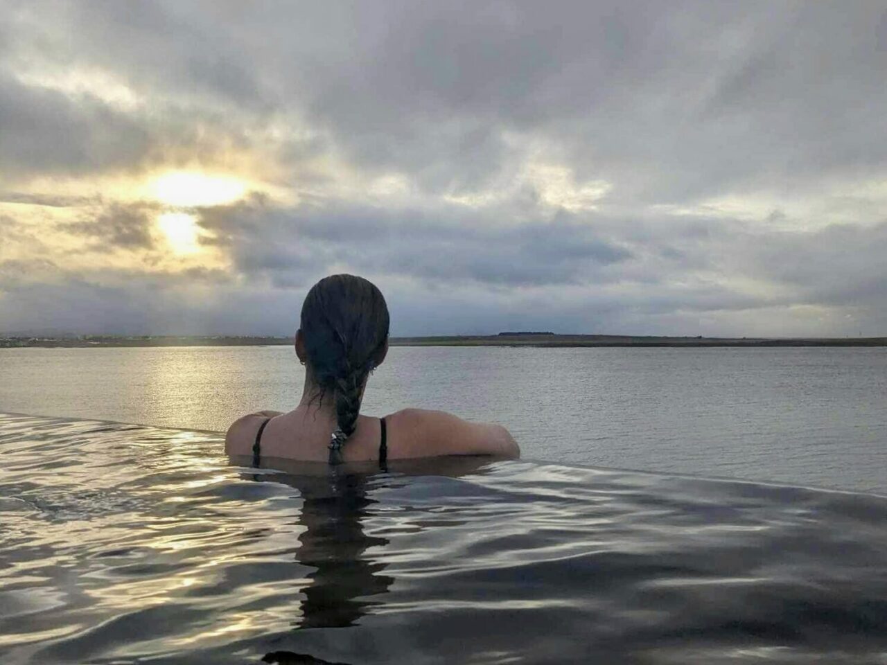 Kvinne står med ryggen til og ser ut over havet. Foto
