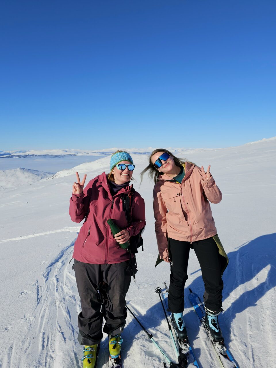 To kvinner med ski på beina smiler inn i kamera. Foto