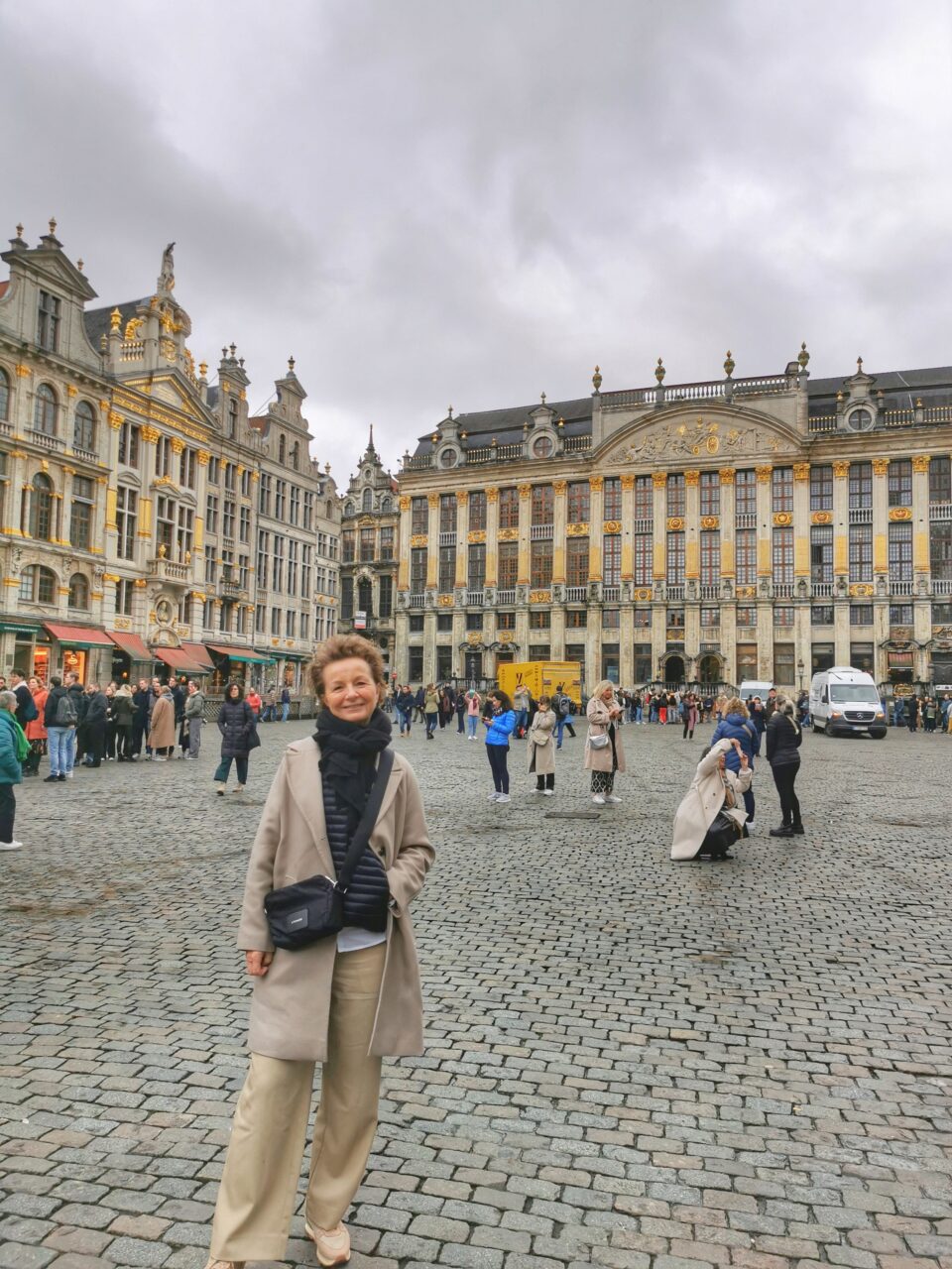 En dame står og smiler på en stor plass (Grand-Place) med bygninger i bakgrunnen. Foto