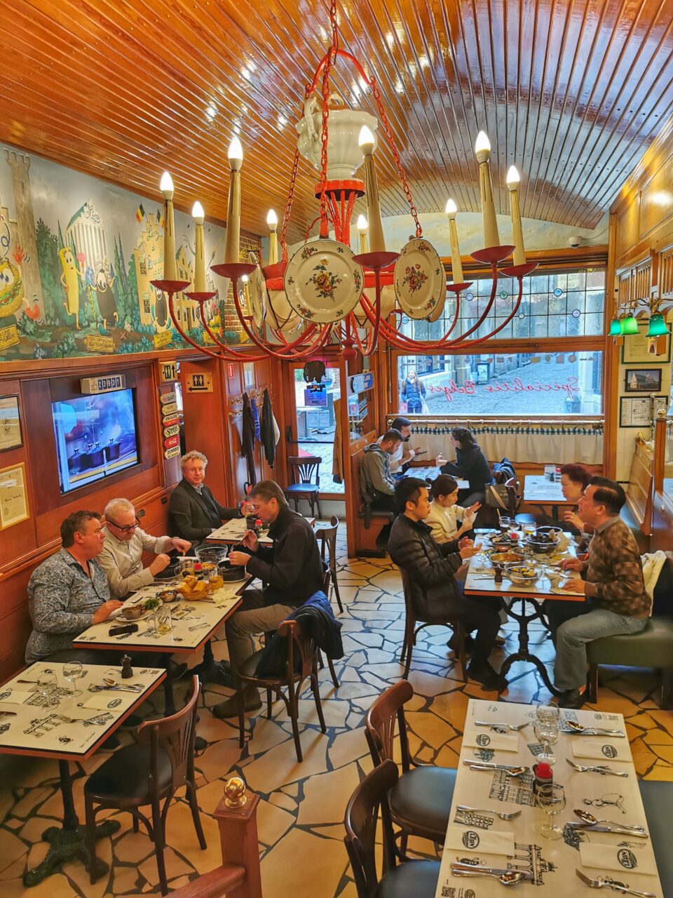 Chez Leon. En restaurant med interiør av tre og rødt. I taket henger en lysekrone med tallerkner til pynt. Foto