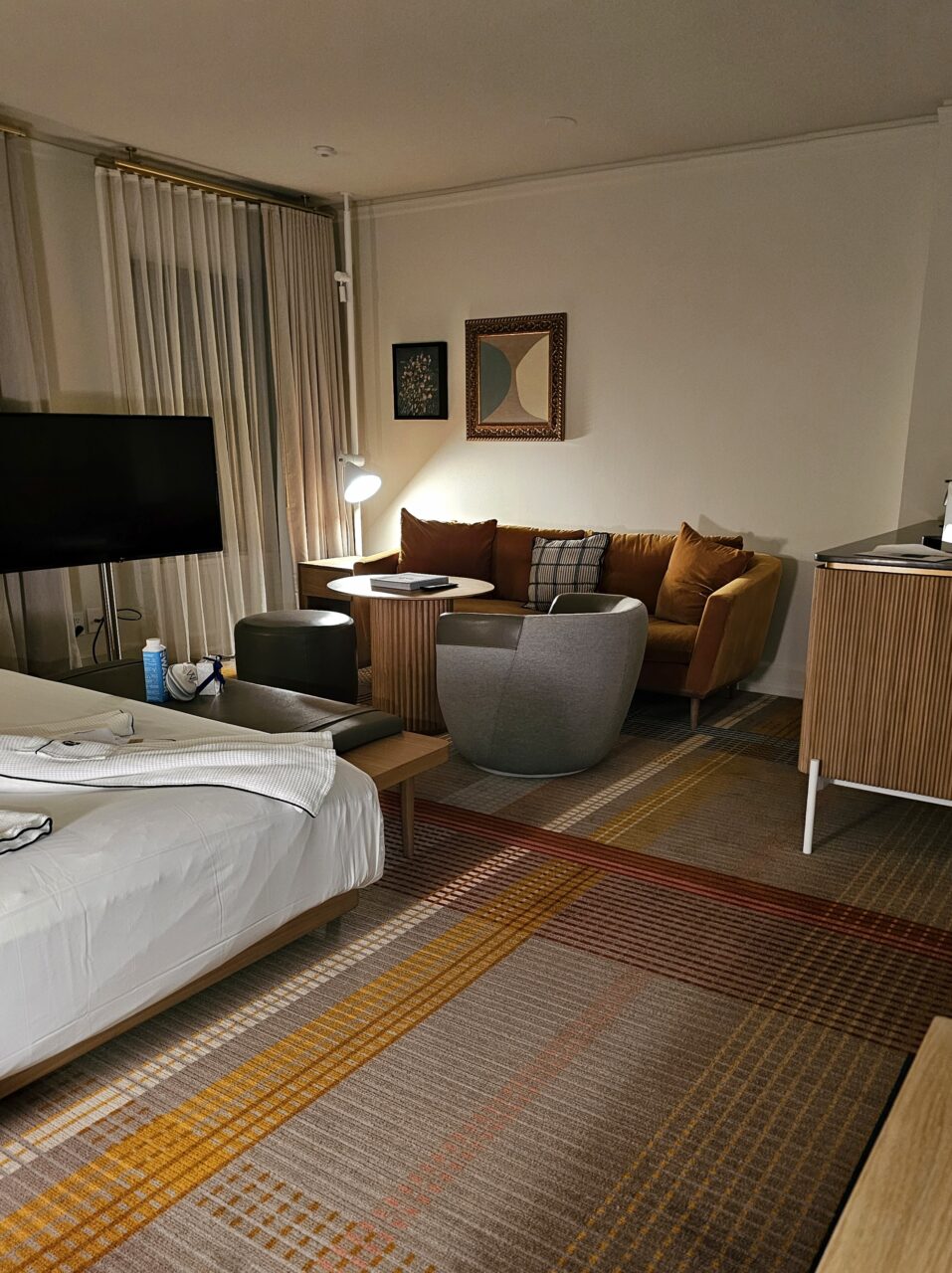 Stort hotellrom med dempet belysning, dobbeltseng og sittegruppe. Foto