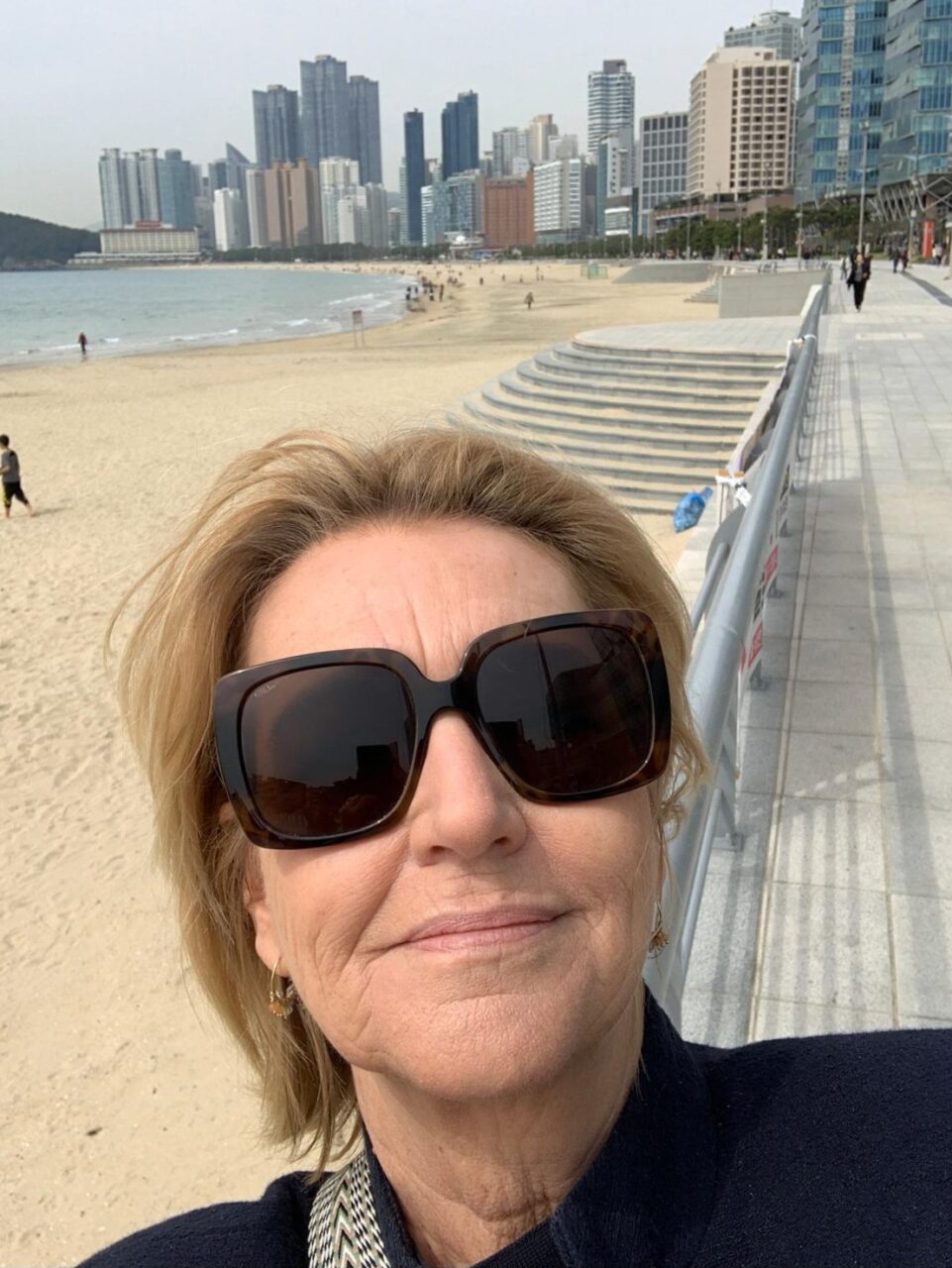 Kvinne med solbriller tar selfie på strand. Foto