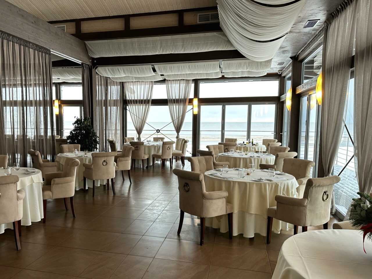 Restaurant med runde bord og utsikt mot sjøen. Foto