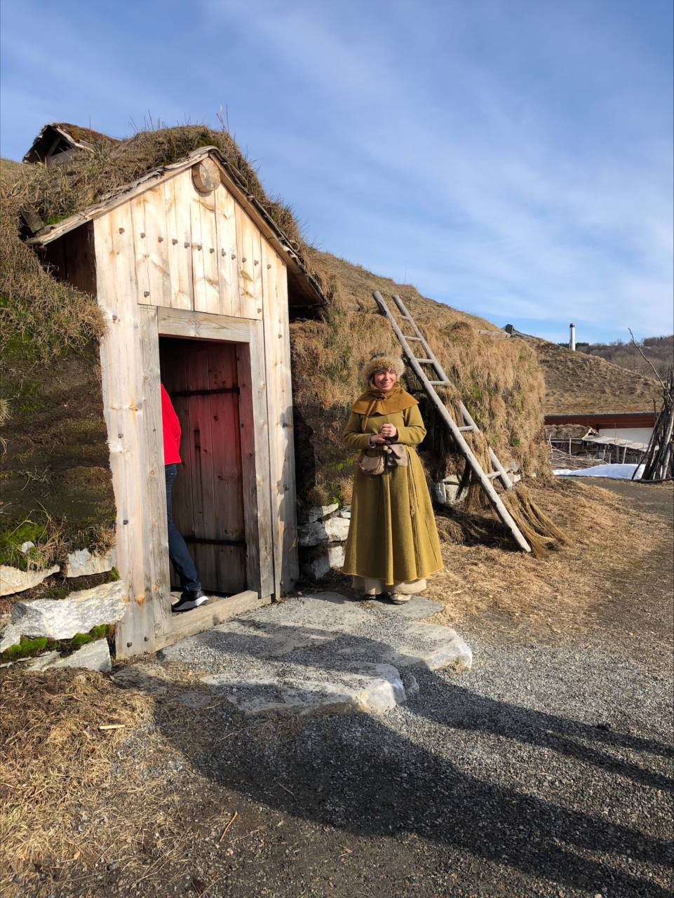 Kvinne i middelalderkostyme står utenfor gammelt hus. Foto