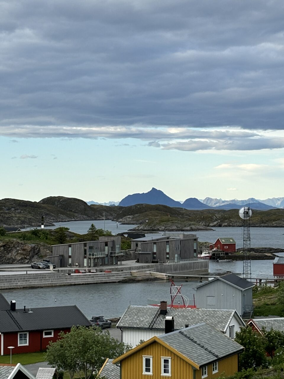 Liten bygd ved sjøen med flotte fjell i bakgrunnen. Foto